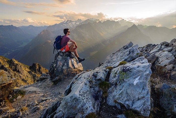 Wanderer sitzt bei Sonnenuntergang auf einem Stein auf einem Berg und schaut in die Weite hinaus.jpg